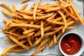 Homemade french fries on parchment paper next to a small cup of ketchup.