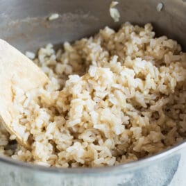A metal saucepan with a spoon and brown rice in it.