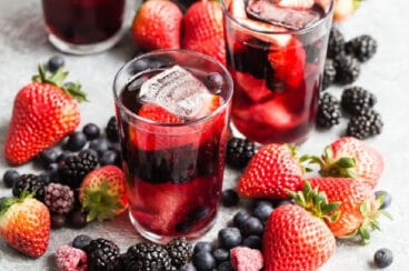 3 glasses and a pitcher of iced tea berry sangria surrounded by piles of fresh berries.