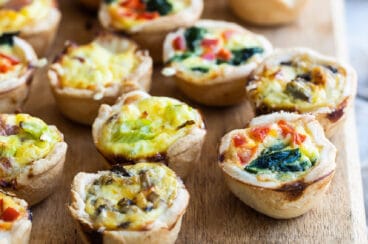 A wooden board filled with 4 varieties of mini quiche.