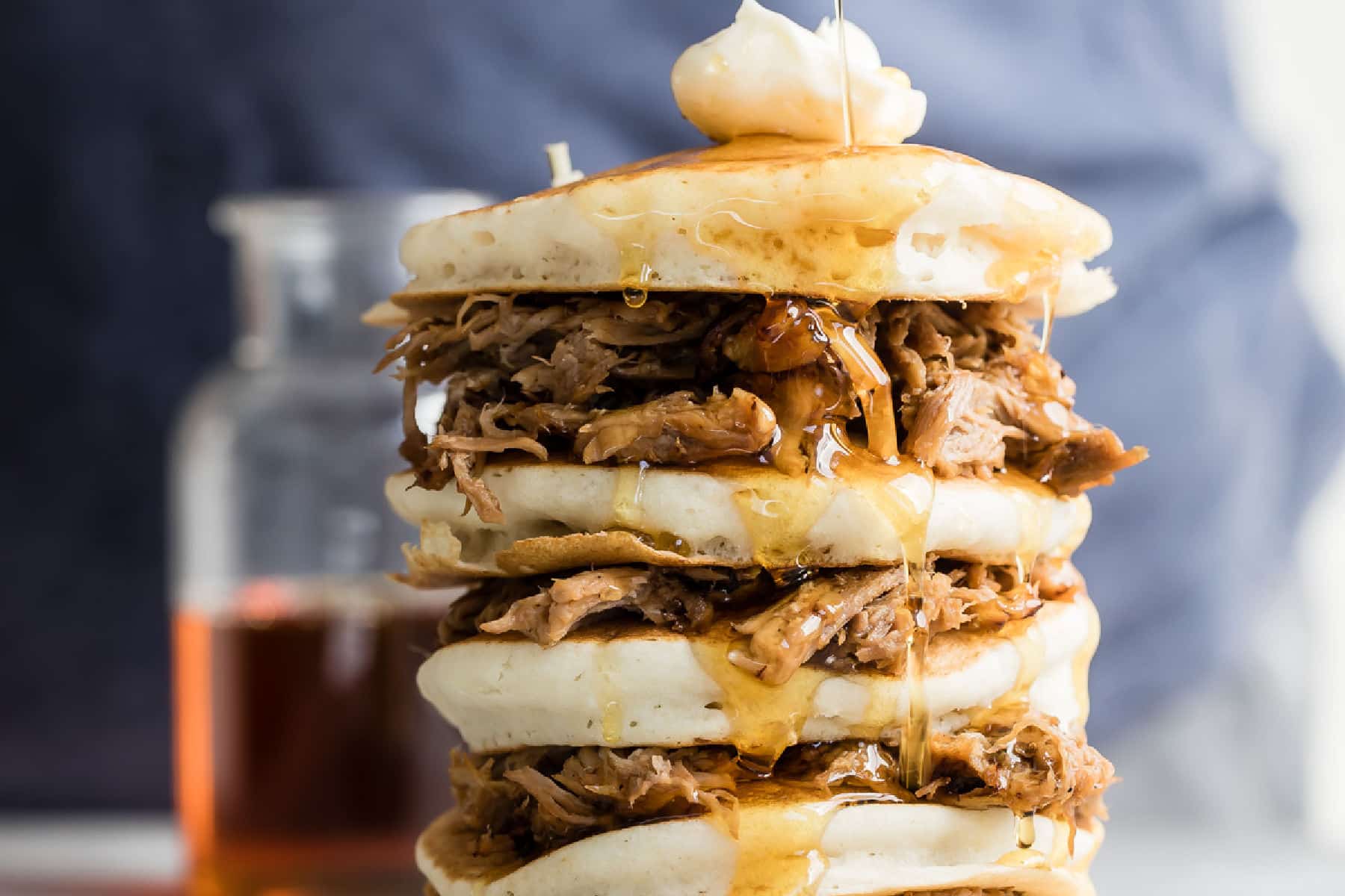 A stack of pulled pork pancakes with butter and whisky maple syrup on top.