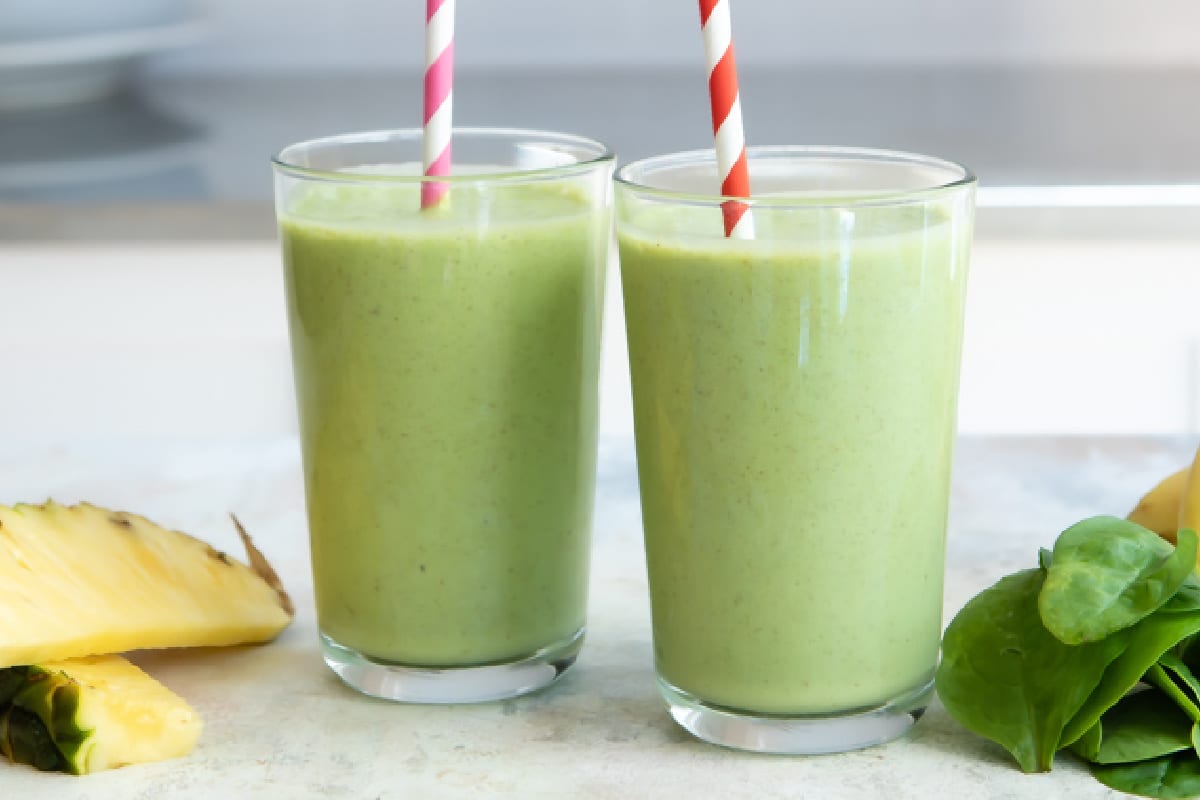 2 glasses of Spinach Smoothie with ingredients nearby.